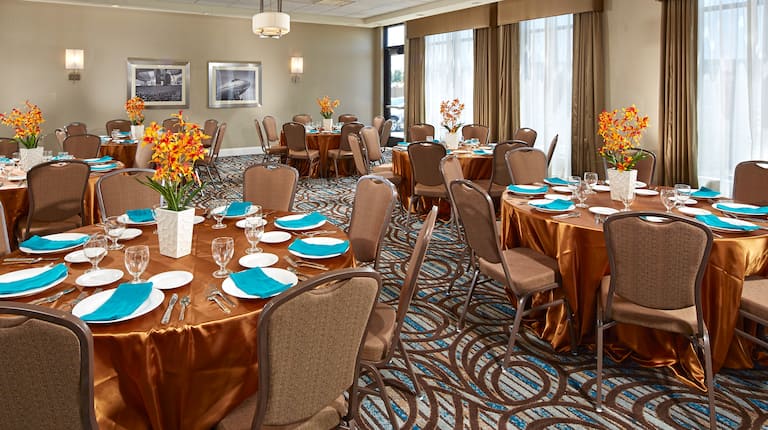 Round Tables With Gold Cloths, Turquoise Napkins, and White Vases With Flowers in Breakwater Banquet Room