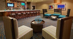 Fully Stocked Lobby Bar With Counter Seating, TVs, and Wall Art and Soft Seating in Lounge Area
