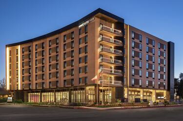 Stunning modern Home2 Suites hotel exterior featuring glowing lights, spacious patio, and dusk sky.