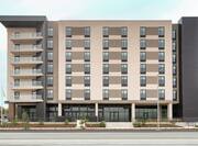 Modern Home2Suites hotel exterior featuring pristine landscaping, outdoor patio, and blue sky.