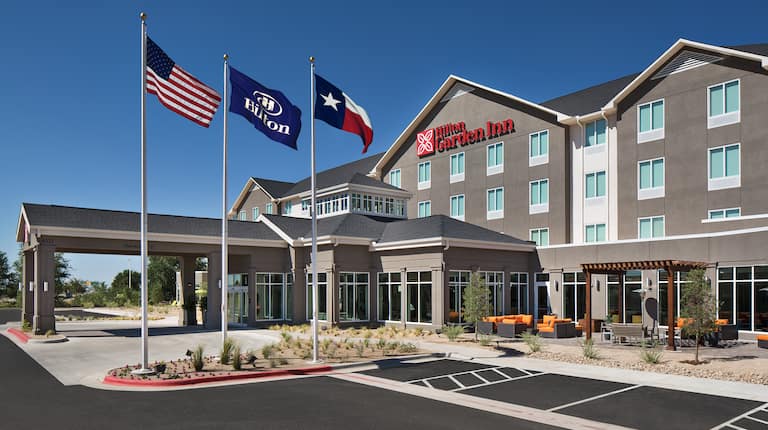 Side View of Hotel Exterior, Circle Driveway, Signage, Flagpoles, Landscaping,  and Parking Lot on Sunny Day
