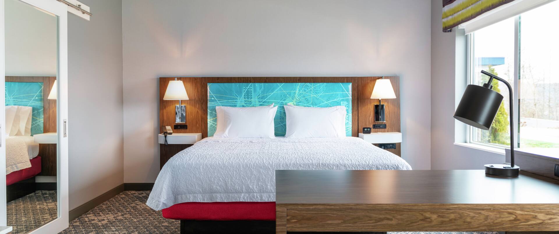 Una amplia suite con cama King, escritorio y silla de un hotel Hampton by Hilton. 