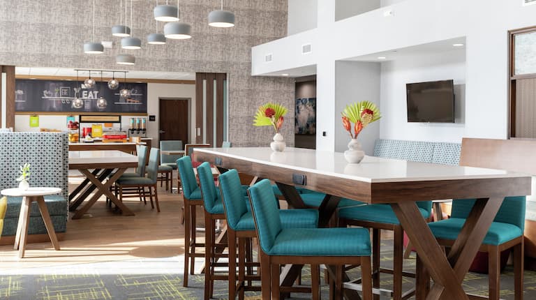 Lobby de un hotel Hampton by Hilton, con sillas y mesas para comer y trabajar. 