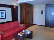Living Area With Wall Art, Red Sofa, Table with Room Service Tray, Wood Cabinet in Corner by Suite Entry Door.
