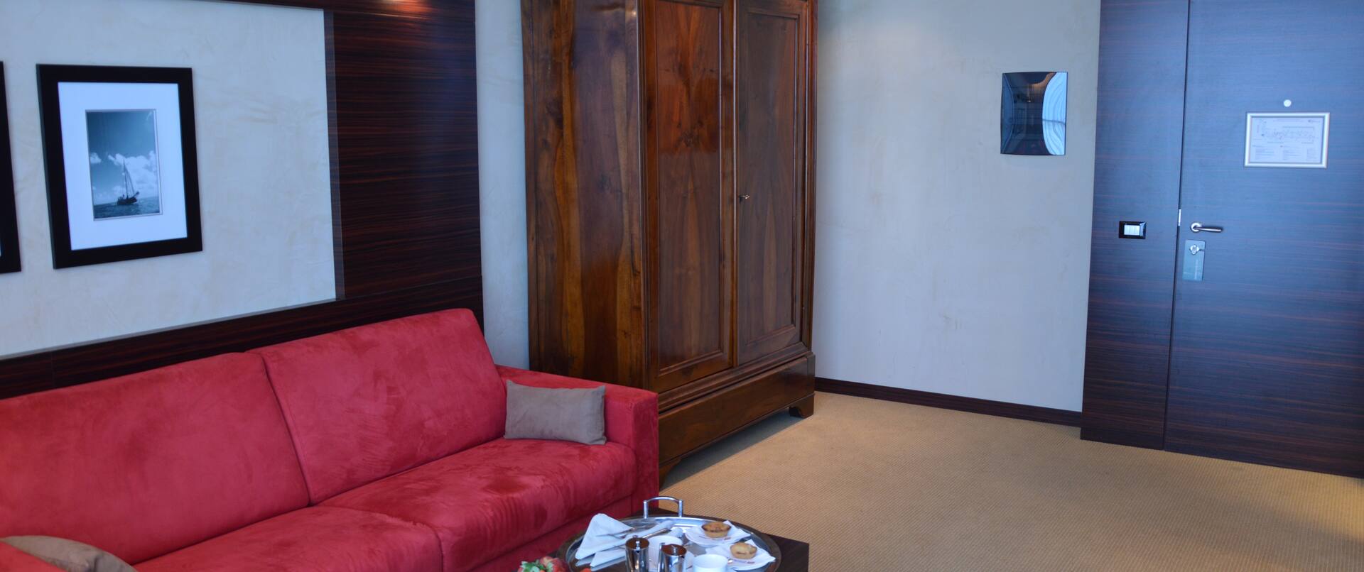 Living Area With Wall Art, Red Sofa, Table with Room Service Tray, Wood Cabinet in Corner by Suite Entry Door.