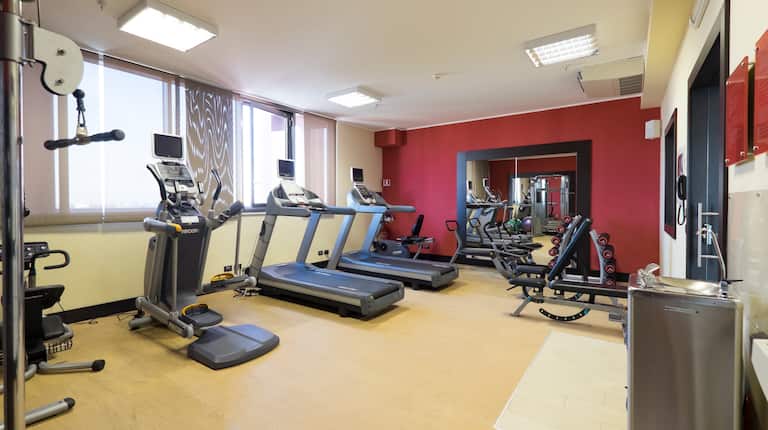 Gym With Weight Bench, Cardio Equipment Facing Large Windows, Large Wall Mirror, Free Weights, and Water Fountain