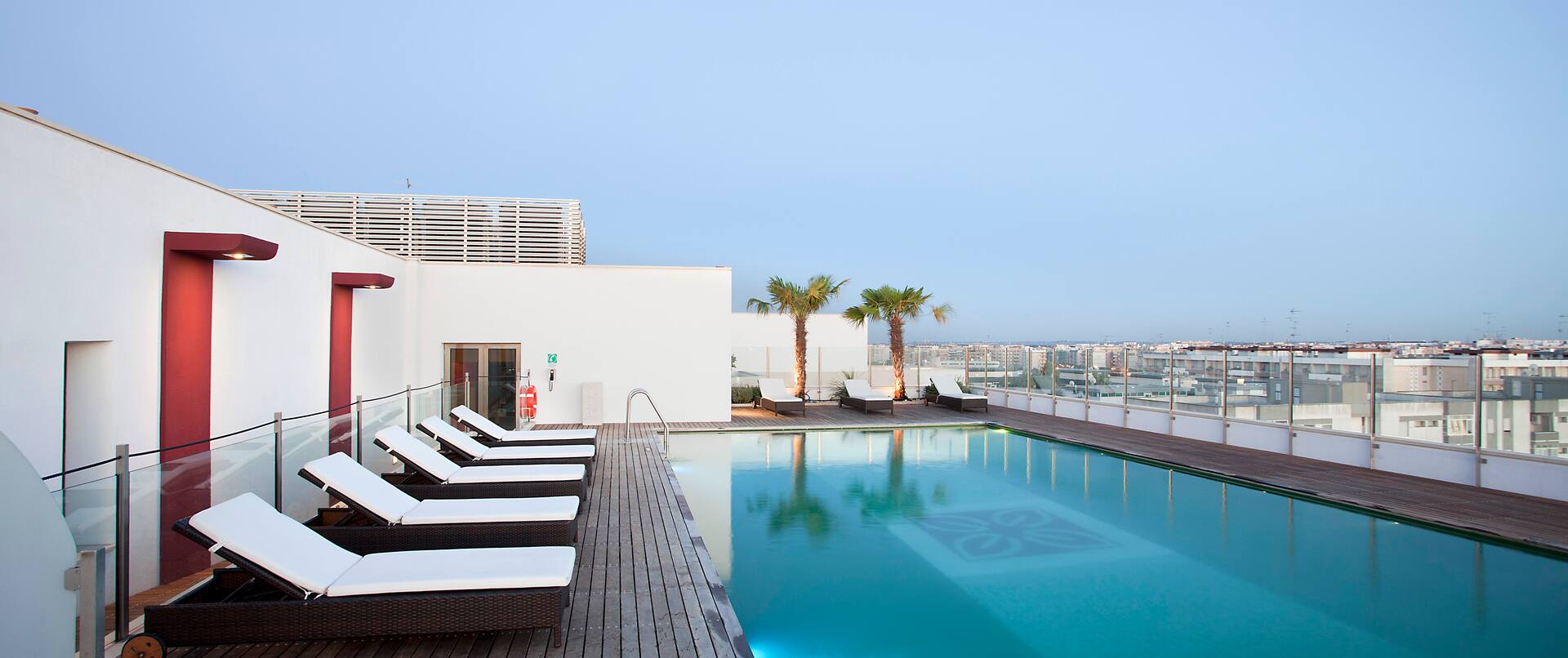 Eight Lounge Chairs by Illuminated Rooftop Pool Overlooking City at Dusk