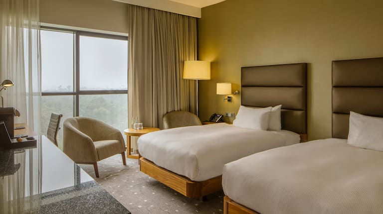 Pokój z dwoma pojedynczymi łóżkami, krzesłami, stołem i oknami z zasłonami