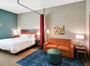 Hotel Studio with a One Bed, Red Drapery Separator between Bed and Orange Sofa with Blue Ottoman