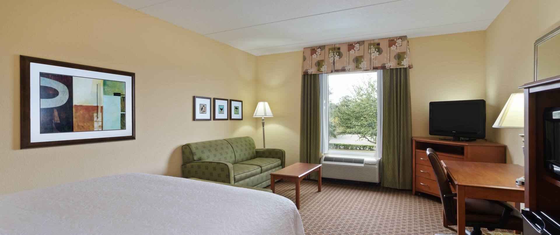 King Bed, Sleeper Sofa, Window With Open Drapes, TV, Work Desk, and Hospitality Center in Study Guest Room