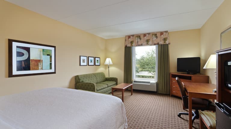 King Bed, Sleeper Sofa, Window With Open Drapes, TV, Work Desk, and Hospitality Center in Study Guest Room