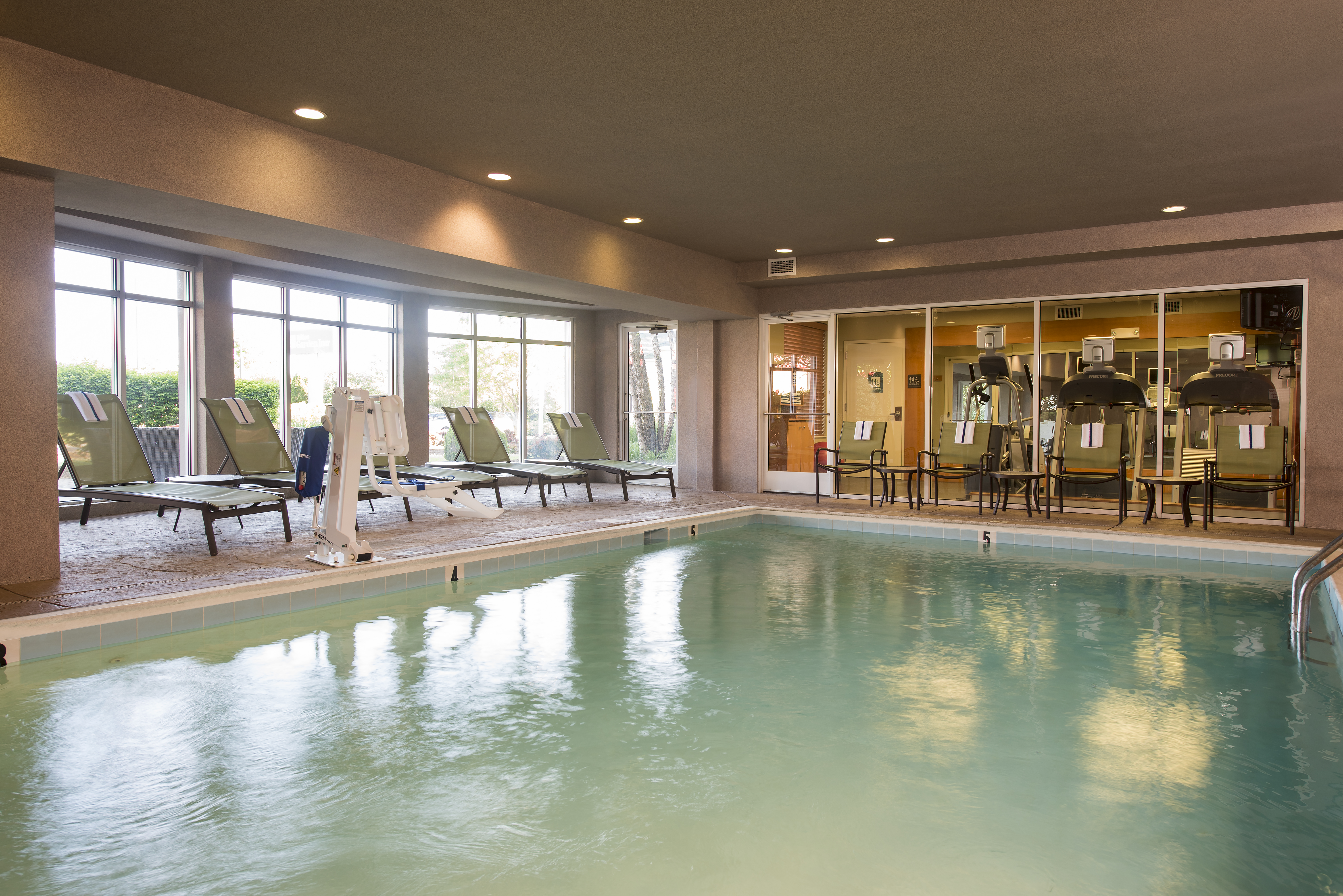 Indoor Pool With Chairs by Windows With Fitness Center View and Lounge Chairs By Windows With Outside Views