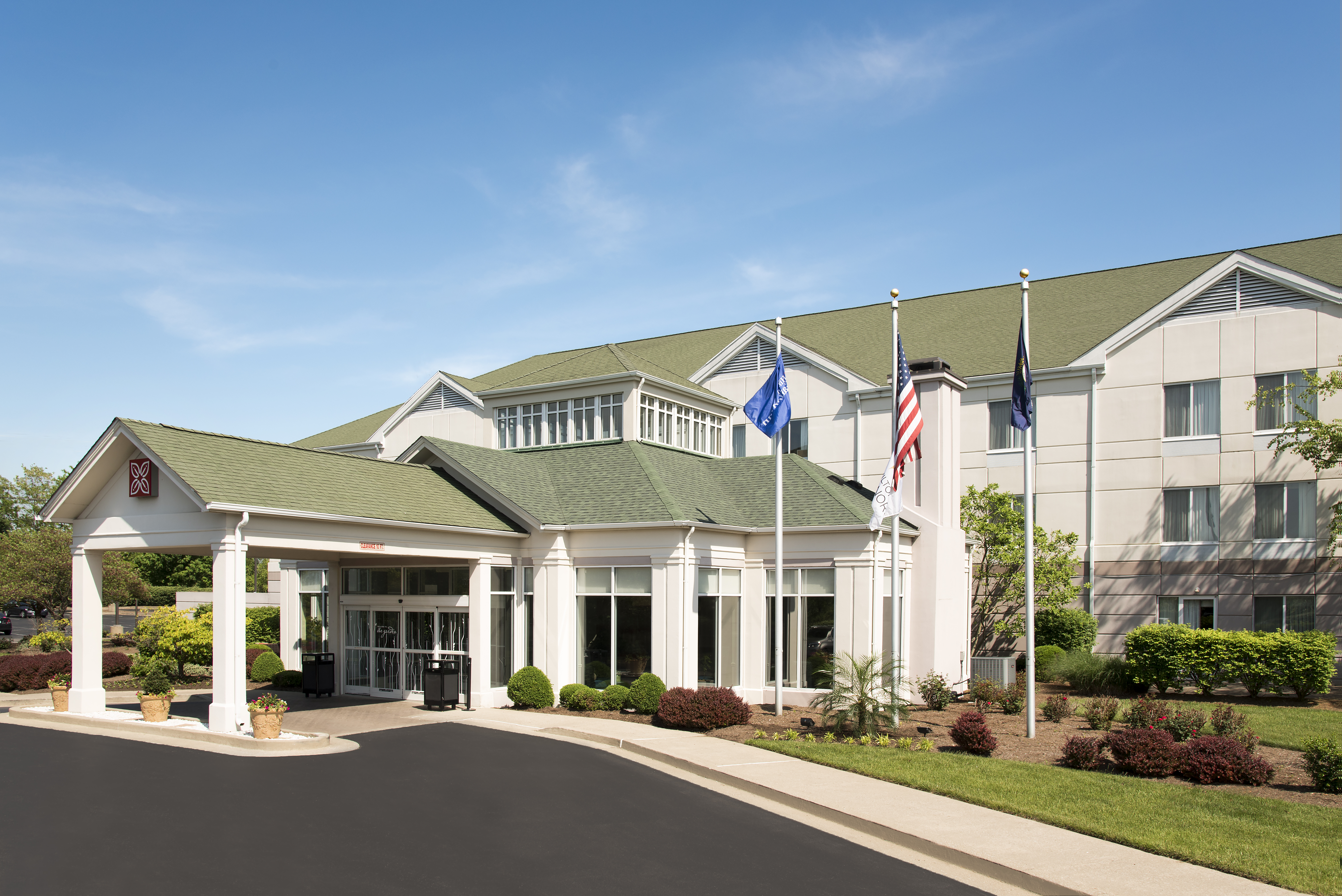 Diagonal View of Hotel Exterior, Entrance Driveway, Landscaping, and Flagpoles