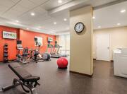 Wall Clock by Door Opening to Laundry Area, Weight Bench, Weight Balls, Cardio Equipment Facing TVs, and Red Exercise Ball in Fitness Center of Spin2 Cycle