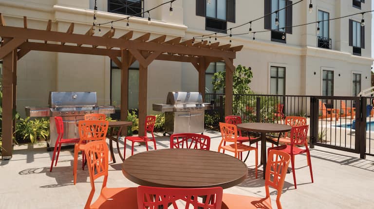 Outdoor Patio With Two Grills Under Wooden Pavilion, Round Tables, Red and Orange Chairs