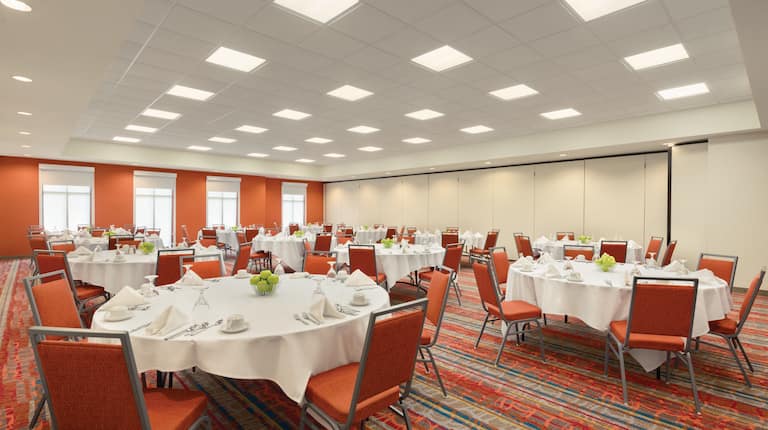 Ballroom With Orange Chairs Around Round Tables With Place Settings on White Linens