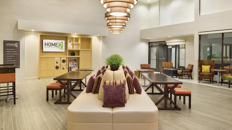 Lobby Seating Around Large Tan Sofa With Tables, Padded Benches, Decorative Lighting, TV, and Additional Seating by Windows