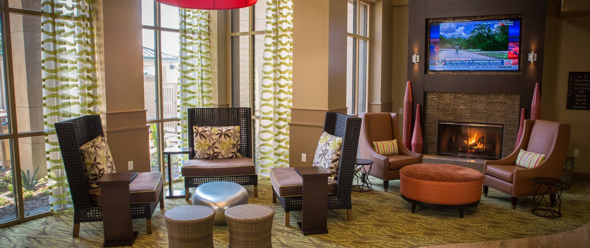 Soft Seating by Windows, and Two Armchairs With Round Ottoman by TV Above Fireplace in Lobby Lounge Area