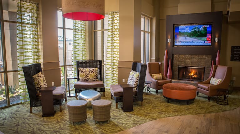 Soft Seating by Windows, and Two Armchairs With Round Ottoman by TV Above Fireplace in Lobby Lounge Area