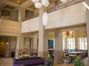View of Soft Seating and Decorative Light Fixtures in Lobby Lounge With Dining Area Seating in Background by Windows 