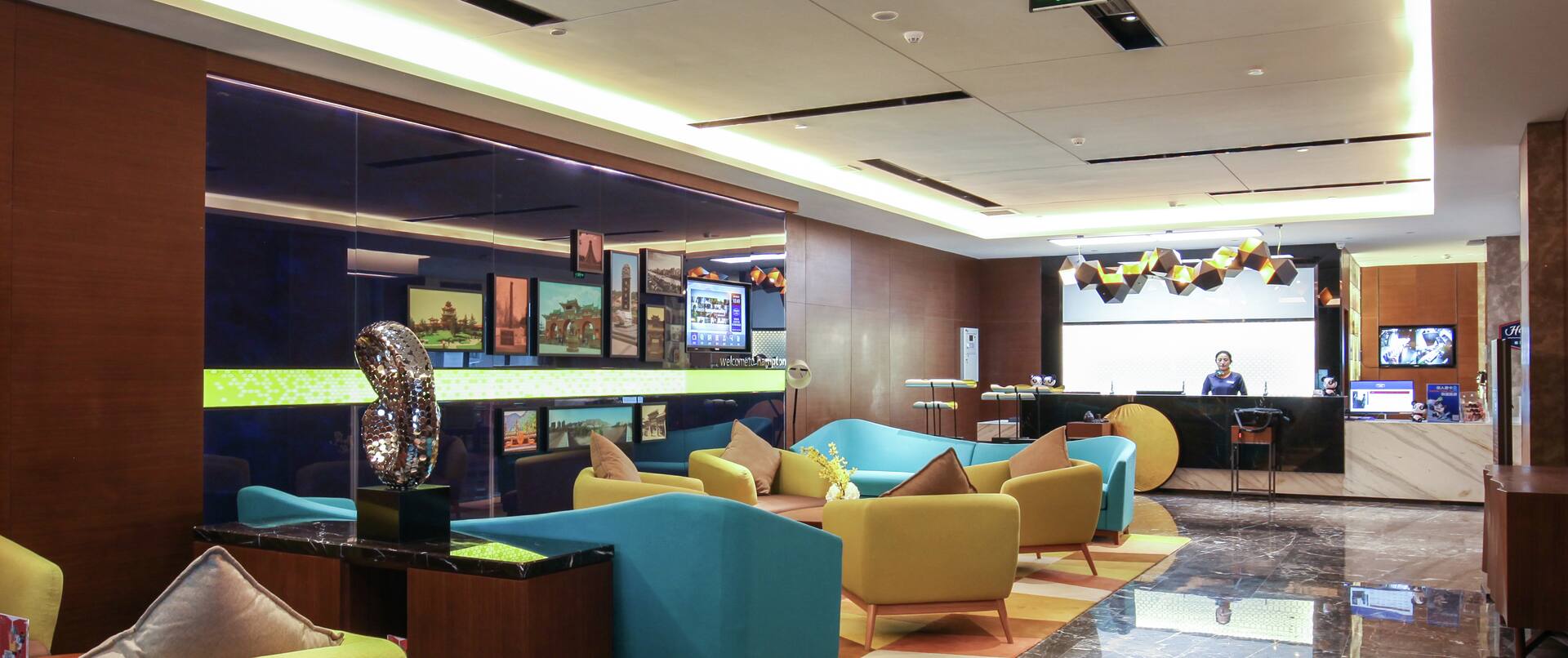 View of Lounge Seating in Lobby and Hampton Staff Member Standing Behind Front Desk