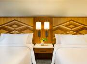 Detailed View of Two Queen Beds With Shared Headboard, Two Illuminated Lamps Above Bedside Table With Fresh Flowers