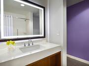 Brightly Lit Vanity Mirror, Fresh Flowers and Amenities by Sink, and Purple Wall in Cottage Bathroom