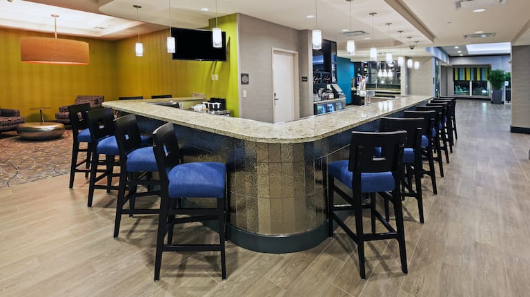 Bar With Blue Chairs at Counter, TV, and Lounge Area With Silver Table and Soft Seating