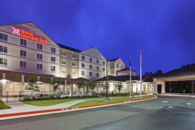 Hotel Exterior, Signage, Driveway, Flag Poles, and Landscaping Illuminated at Night