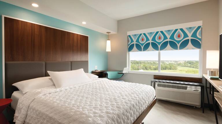 Guest room showing bed with white linens, blue wall, and patterned window covering