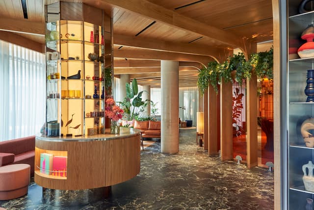 Hotel lobby with hardwood ceiling and support pillars, as well as soft seating and a display counter with glass art and pottery..