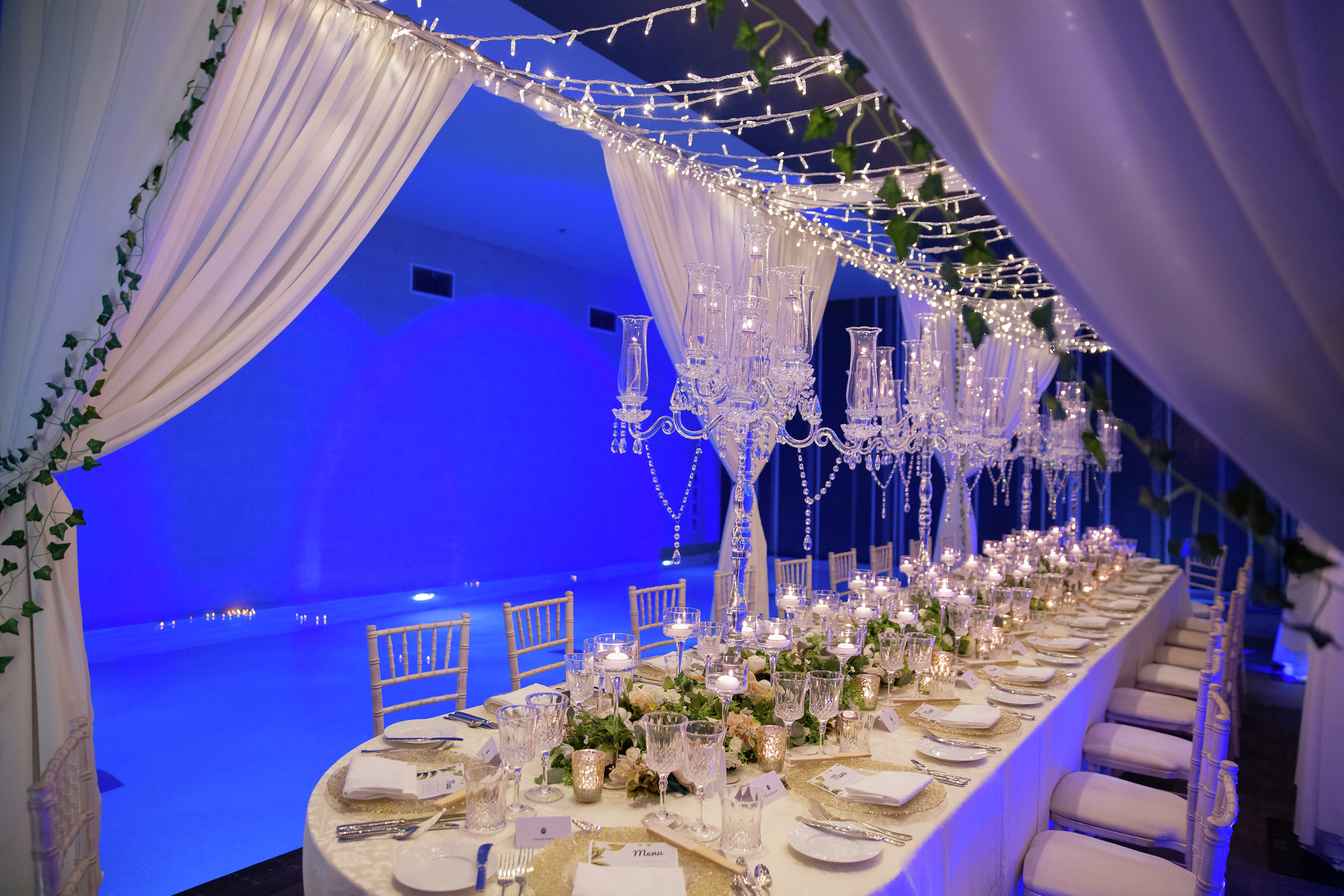 a long dining table with flowers and candles beside a pool