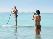 a woman taking a photo of a man on a paddle board