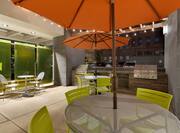 Two Round Tables with Orange Umbrellas, Green Chairs and Two Grills on Illuminated Outdoor Patio at Night