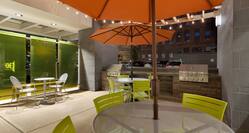 Two Round Tables with Orange Umbrellas, Green Chairs and Two Grills on Illuminated Outdoor Patio at Night