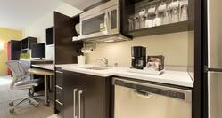 Kitchen With Fridge, Dishwasher, Microwave Above Sink, Dinnerware in Wood Cabinets, Work Desk, and TV in King Studio Suite
