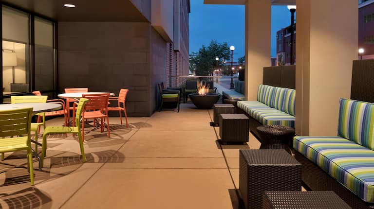 Illuminated Outdoor Lounge With Tables, Striped Sofas and Round Fire Pit at Dusk