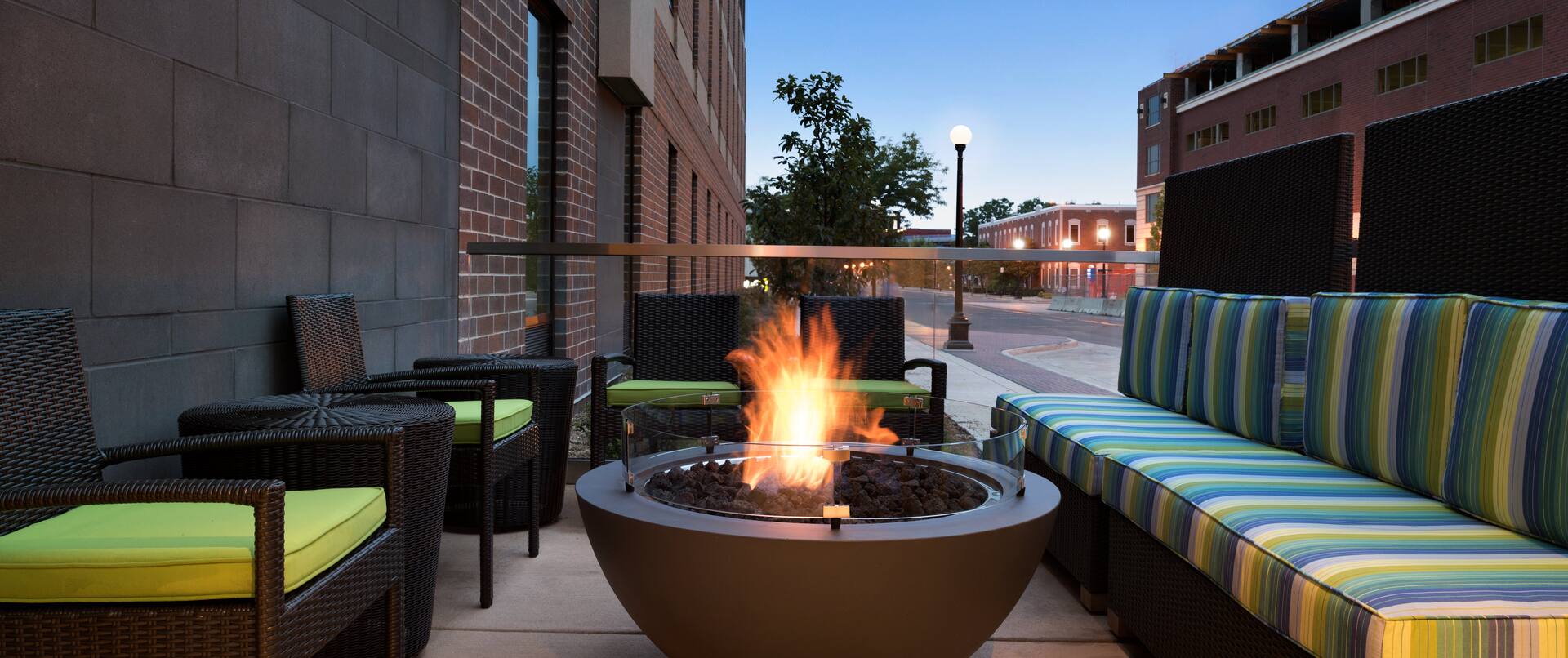 Outdoor Lounge With Cushioned Armchairs, Round Fire Pit, and Striped Sofas at Dusk