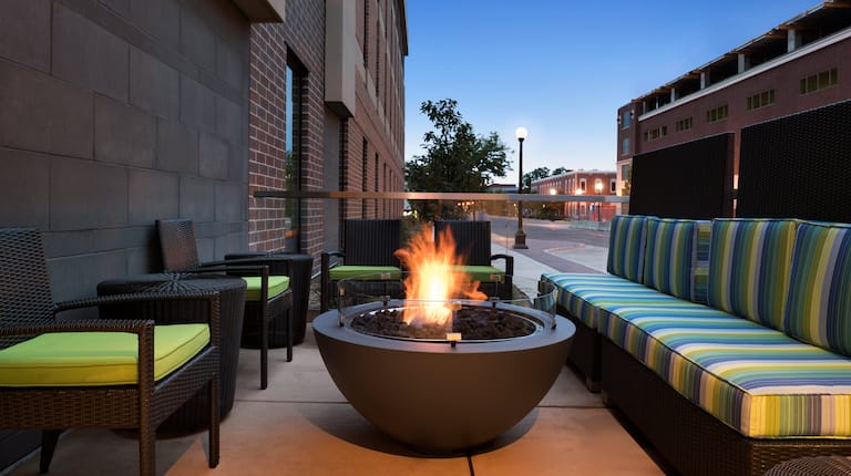 Outdoor Lounge With Cushioned Armchairs, Round Fire Pit, and Striped Sofas at Dusk