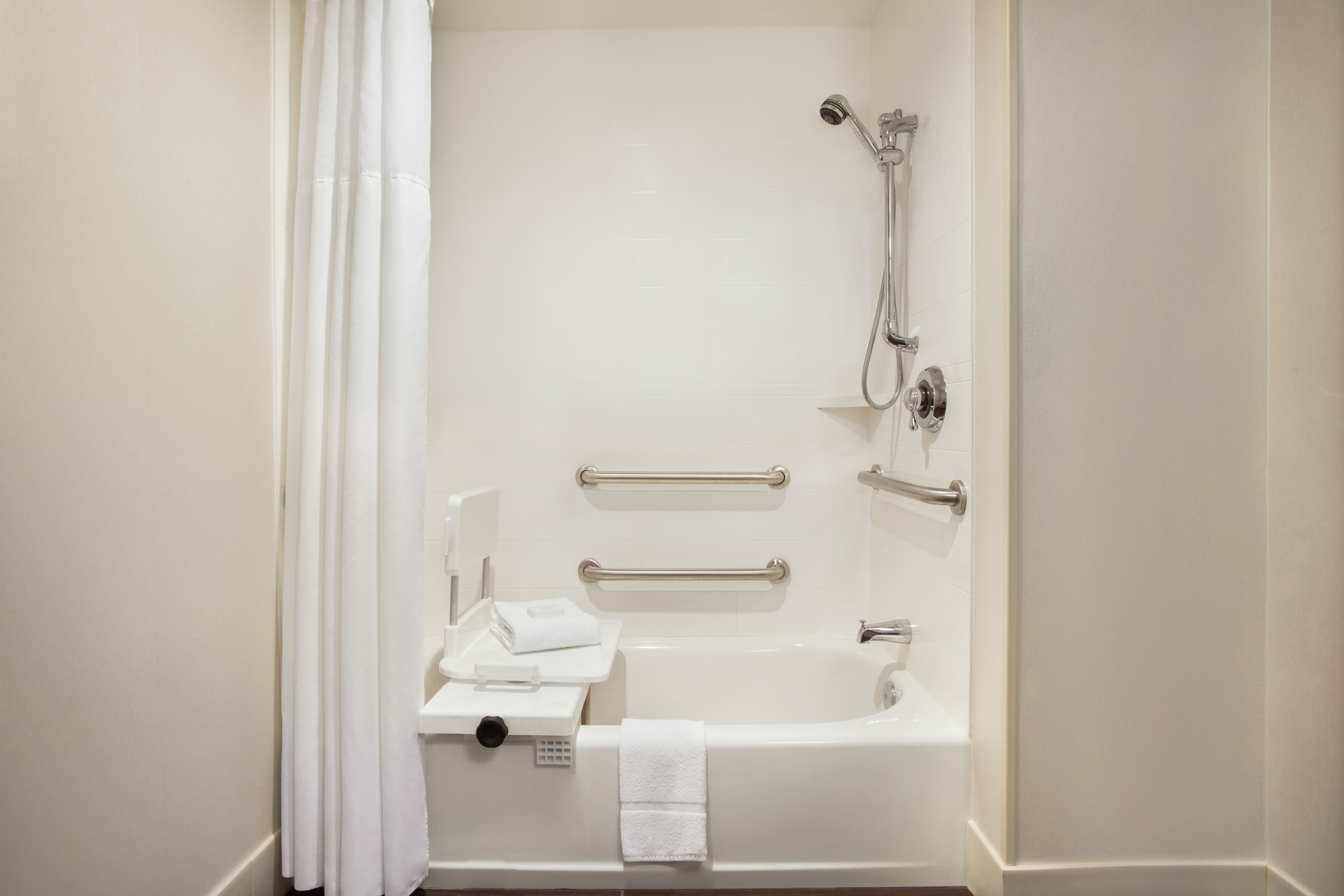 Spacious accessible tub featuring seat, grab bars, and lowered shower head.