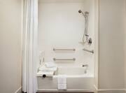 Spacious accessible tub featuring seat, grab bars, and lowered shower head.