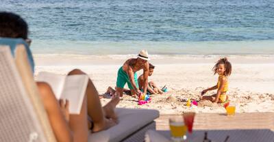 Dad and kids digging in the sand as mom reads a book at Rose Hall Resort & Spa, an all-inclusive resort.