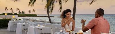 Woman and man having dinner on a patio overlooking the sea at Hilton Rose Hall Resort & Spa, an all-inclusive resort.
