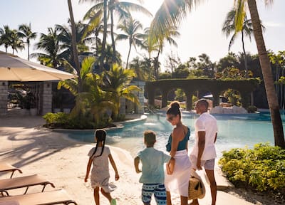 Family of four walks along side of pool under palm trees at Hilton Rose Hall Resort & Spa, an all-inclusive resort.