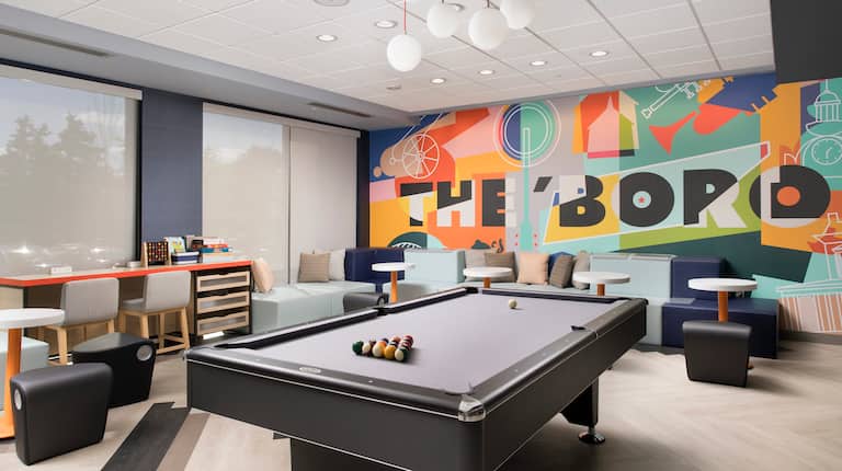 Game Area With Pool Table, Tables, Chairs, Windows, and Colorful Wall Mural