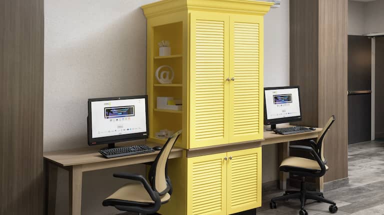 Yellow Storage Cabinet Between Two Computers on Long Desk, and Two Ergonomic Chairs in Business Center