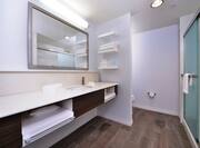 Sink, Toiletries, Amenities, Vanity Mirror, Towels, Toilet Behind Partition, and Shower With Glass Doors in Guest Bathroom