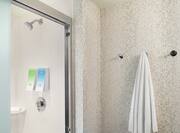 Bright guest room bathroom featuring walk in shower with bathroom amenities and towel hanging on wall.