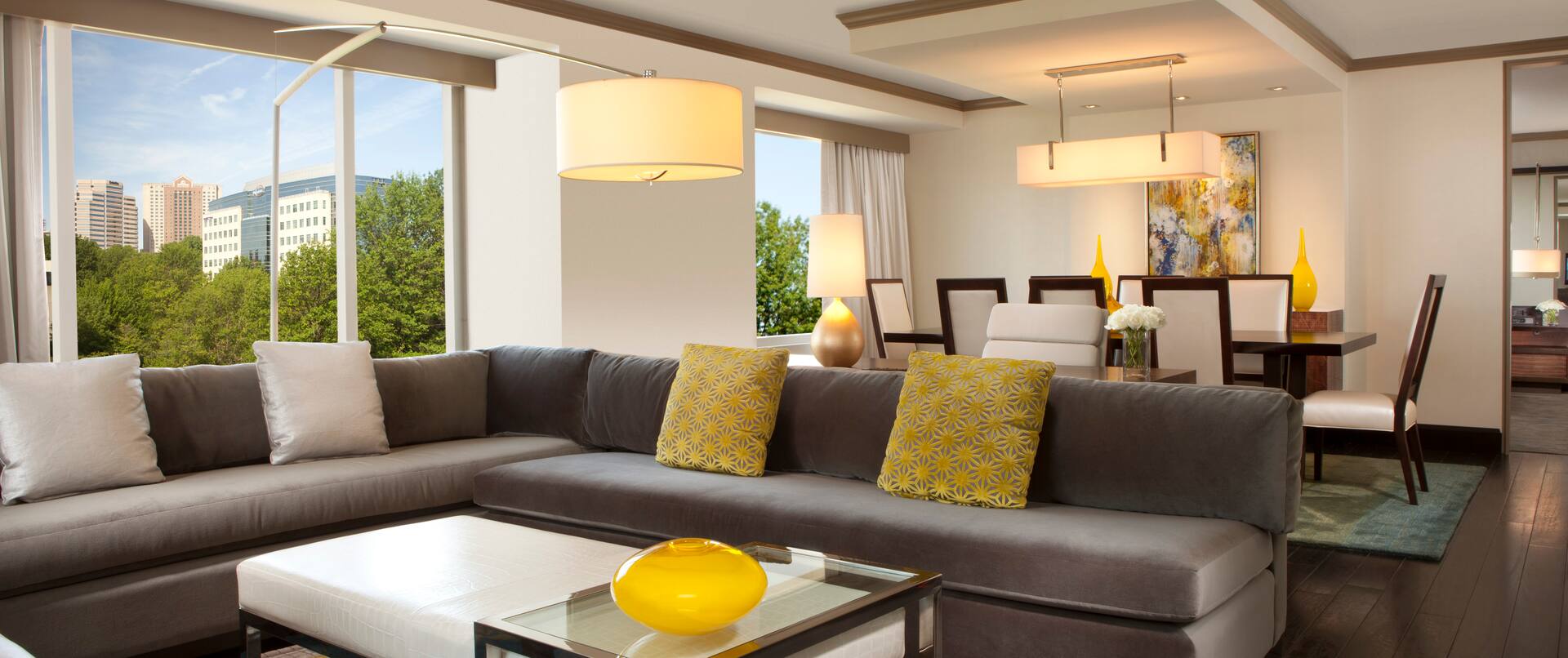 Deluxe Suite Living Area with L-Shaped Sofa, Dining Table and Chairs, and Floor-to-Ceiling Windows with Outdoor View