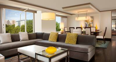 Deluxe Suite Living Area with L-Shaped Sofa, Dining Table and Chairs, and Floor-to-Ceiling Windows with Outdoor View